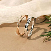 Rose gold and white gold crossover twist couple rings with diamonds, laid on soft beige fabric, modern design